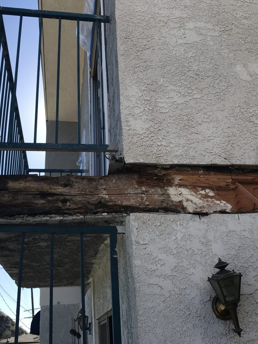 Rust and decay on a metal balcony structure attached to a stucco wall.