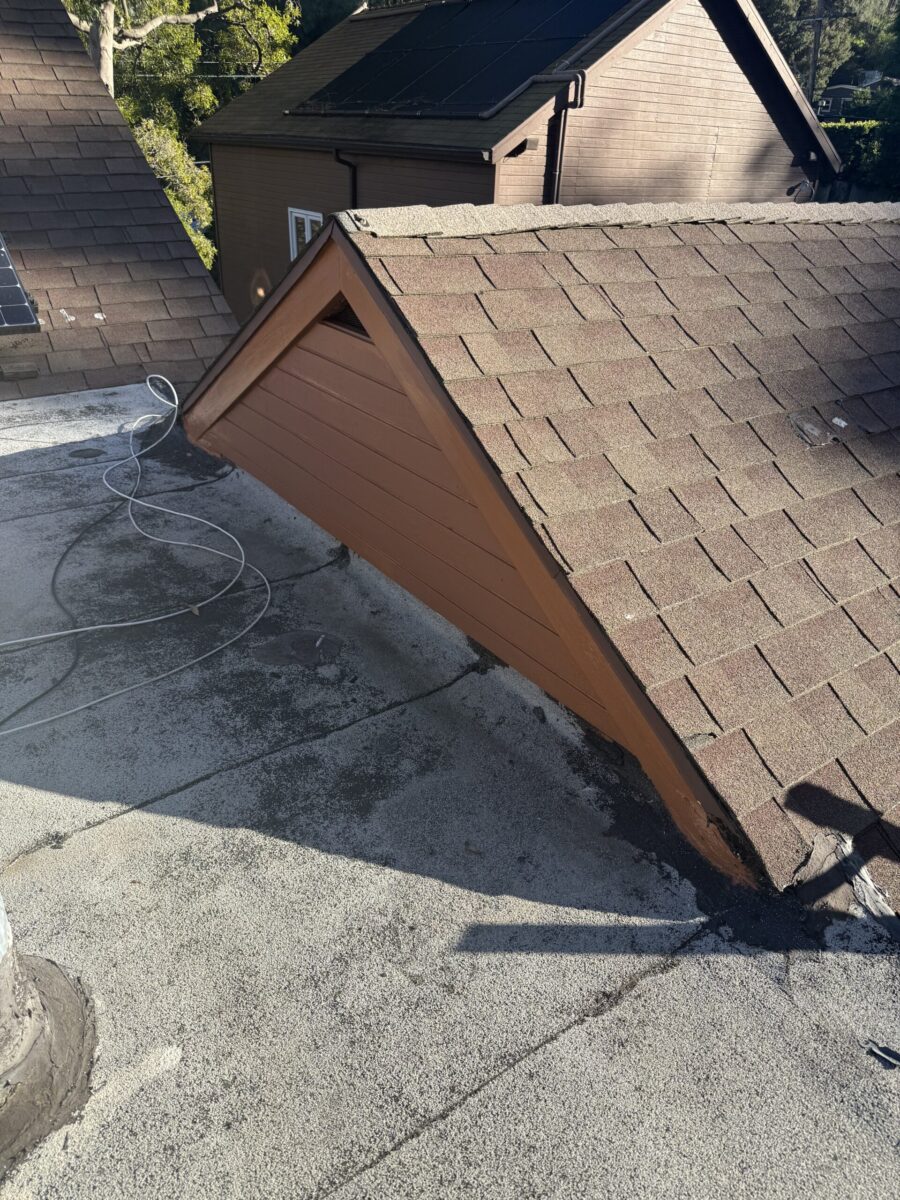 A small wooden doghouse on a concrete surface with a shingled roof.