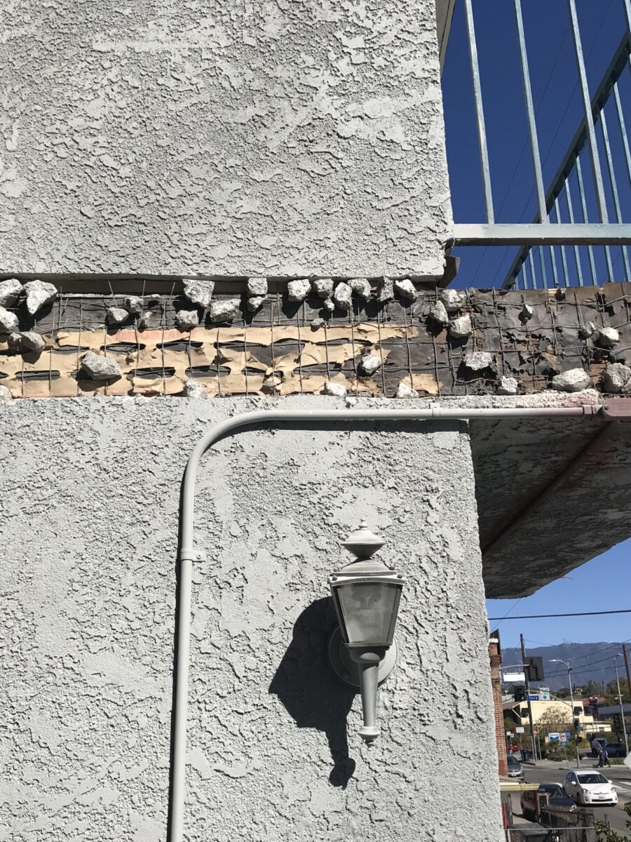 A weathered brick and concrete structure with a wall-mounted lantern under a solar panel array.
