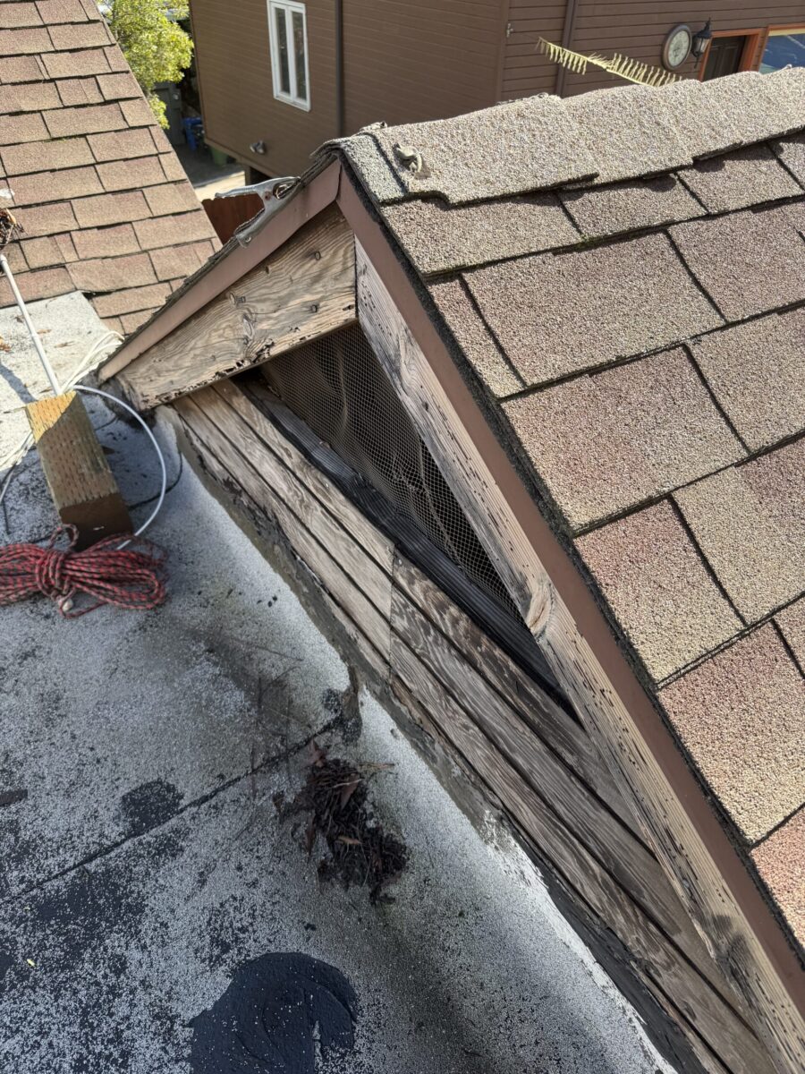Damaged roof section with exposed wooden beams and missing shingles.