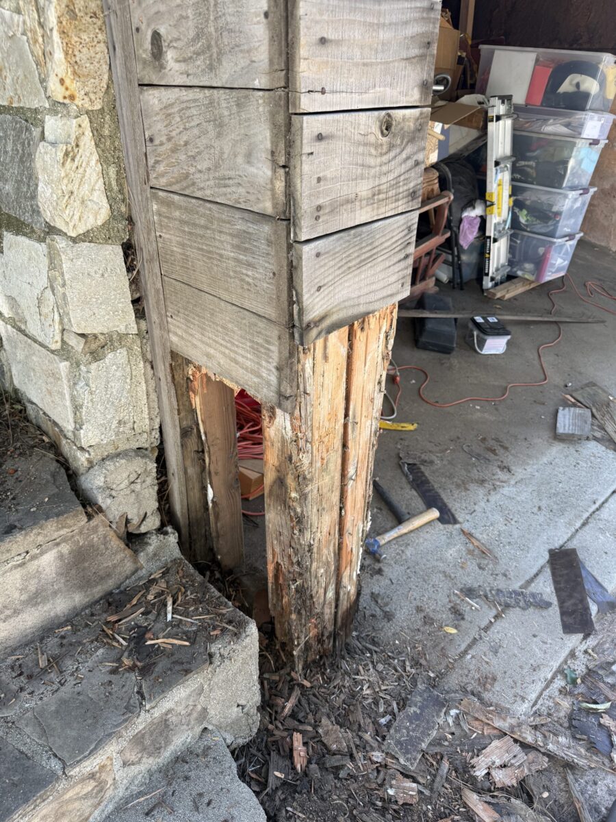 A wooden pillar with severe rot and damage at its base.
