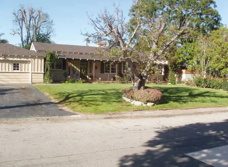 Single-story house with a large tree in front yard on a sunny day.