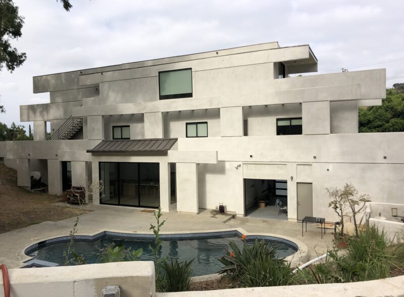 Modern concrete house with a pool under a cloudy sky.