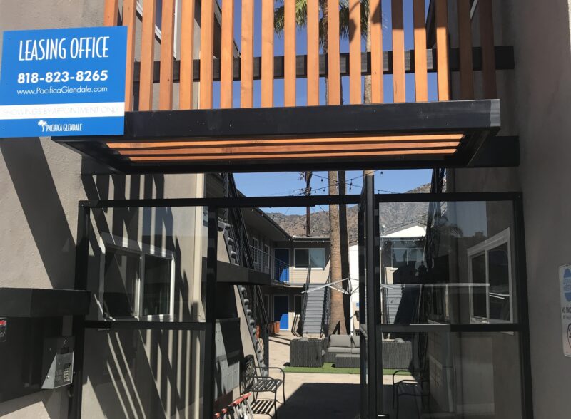A narrow alley with a blue business sign and shadows cast by stairs.