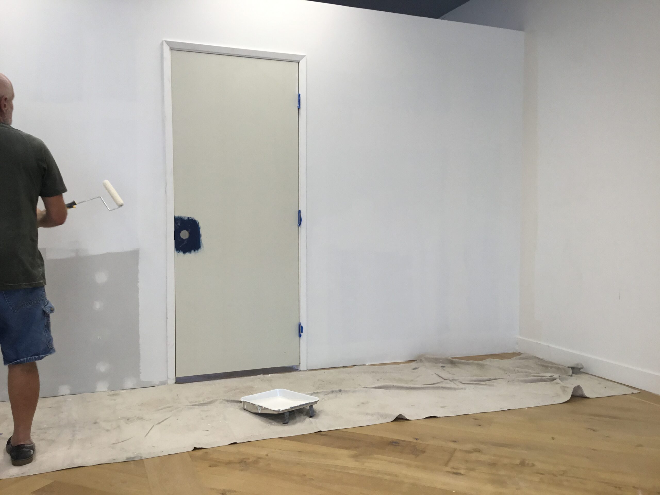 A plain white door in a minimally furnished room with a paint tray on the floor.