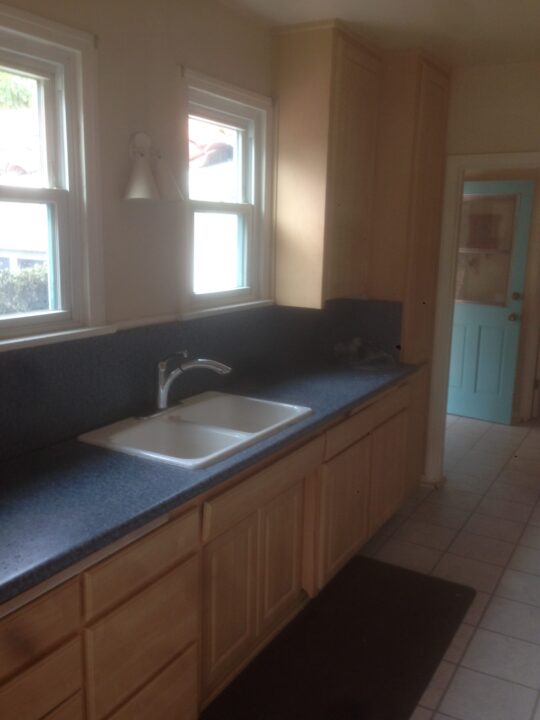 Kitchen sink area with wooden cabinets and blue countertop under two windows. Kitchen sink area with wooden cabinets and blue countertop under two windows.