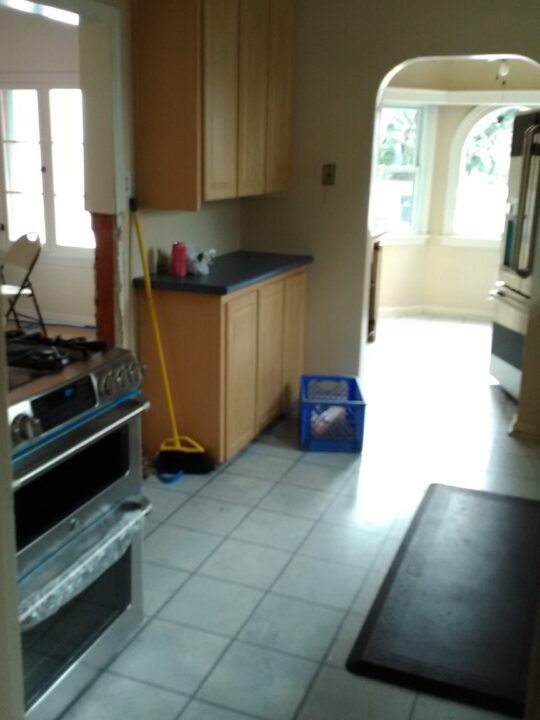 A narrow kitchen with tiled floors and a stove on the left. A narrow kitchen with tiled floors and a stove on the left.