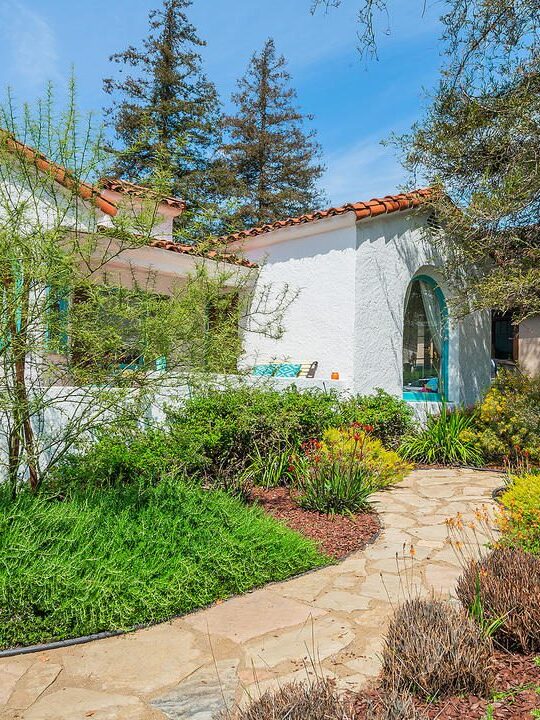 Charming garden path leading to a Mediterranean-style white house with red roof tiles. Charming garden path leading to a Mediterranean-style white house with red roof tiles.