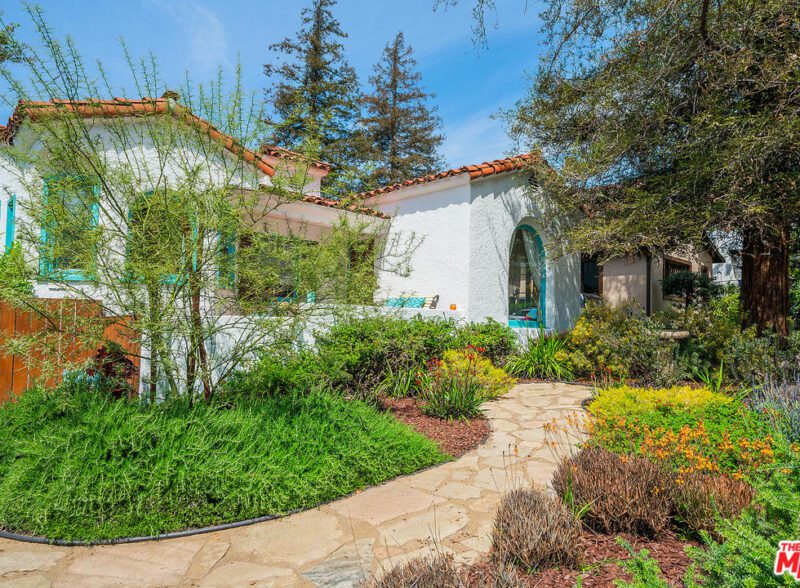 Charming garden path leading to a Mediterranean-style white house with red roof tiles.
