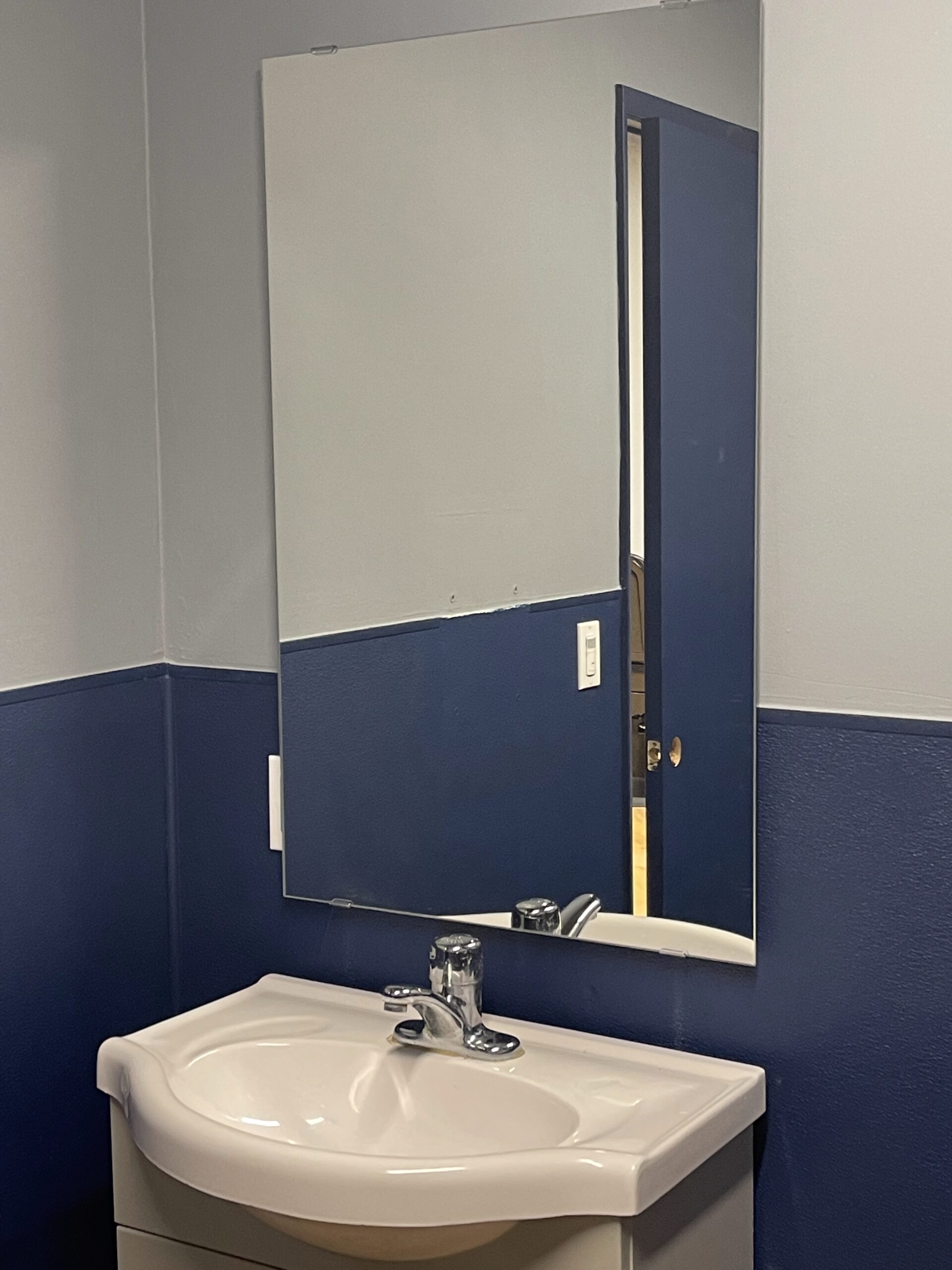 A modern bathroom sink with a mirror and navy blue walls.