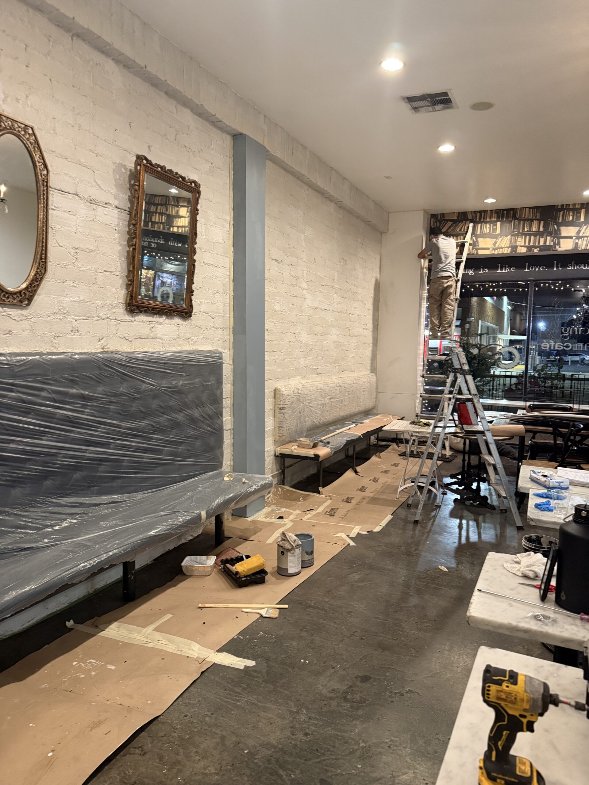 Indoor space undergoing renovation with plastic-covered furniture and painting supplies.