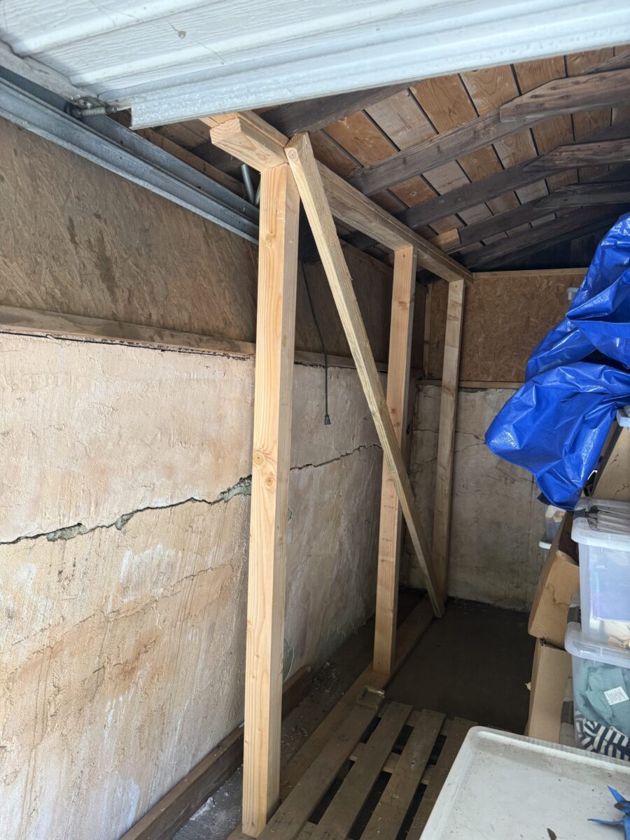 Wooden support beams brace a cracked wall in a storage area.