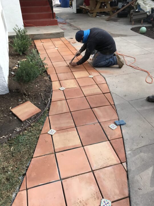 Worker installing curved terracotta tiles on a pathway. Worker installing curved terracotta tiles on a pathway.
