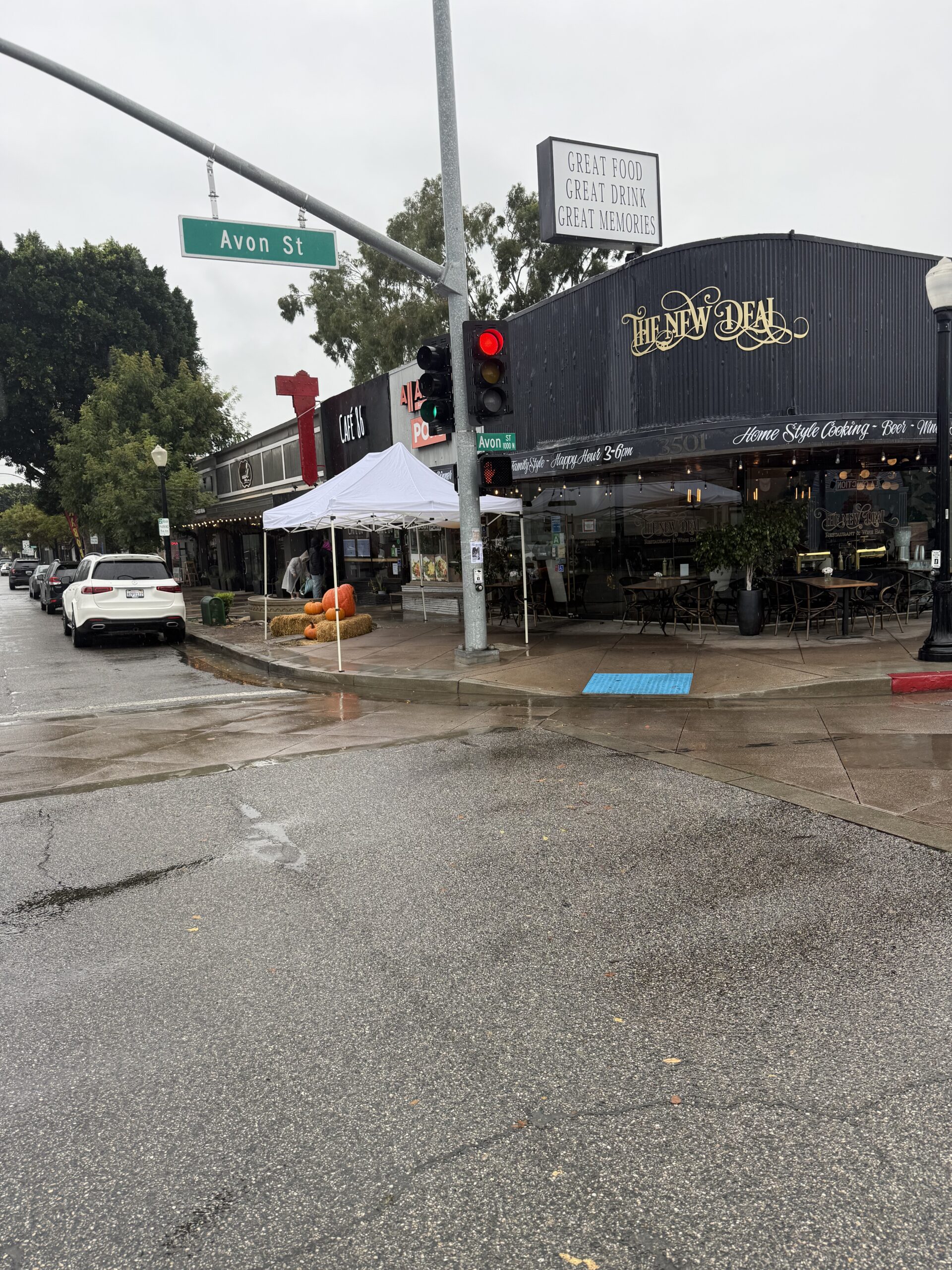 A rainy street corner with a restaurant named Honey Salt and cars passing by.