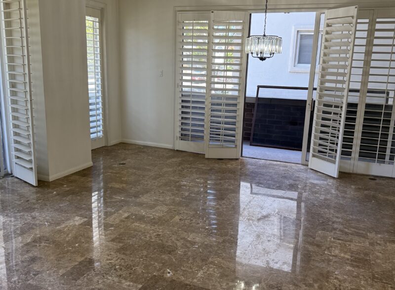 Empty room with polished marble floor and large windows with shutters.